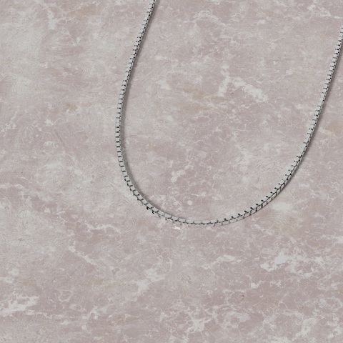 Silver chain necklace on a textured beige surface