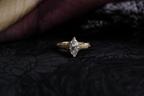 Victorian Inspired gold ring with a marquise Lab diamond on a dark textured fabric background